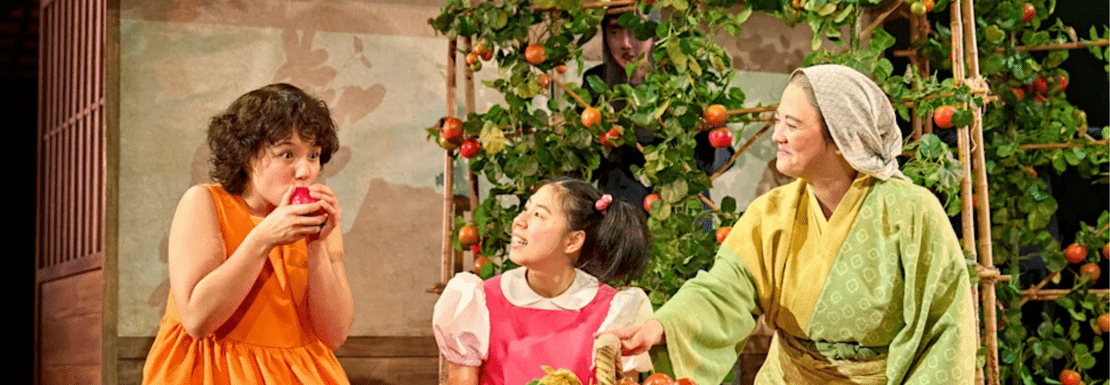 Actors eating fruit in a sunny garden in the My Neighbour Totoro stage show