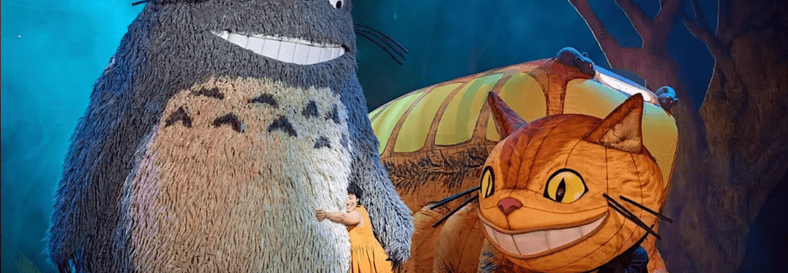 An actor hugging giant puppets on stage in My Neighbour Totoro