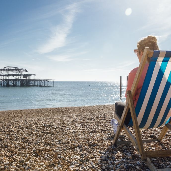 Rear view of woman sitting in striped deckchair on the beach