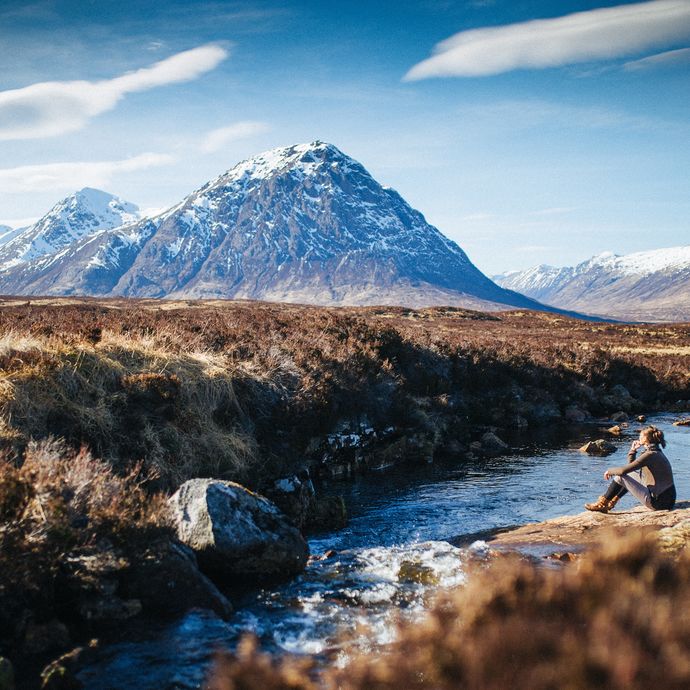 Person sat beside a stream enjoying mountain view