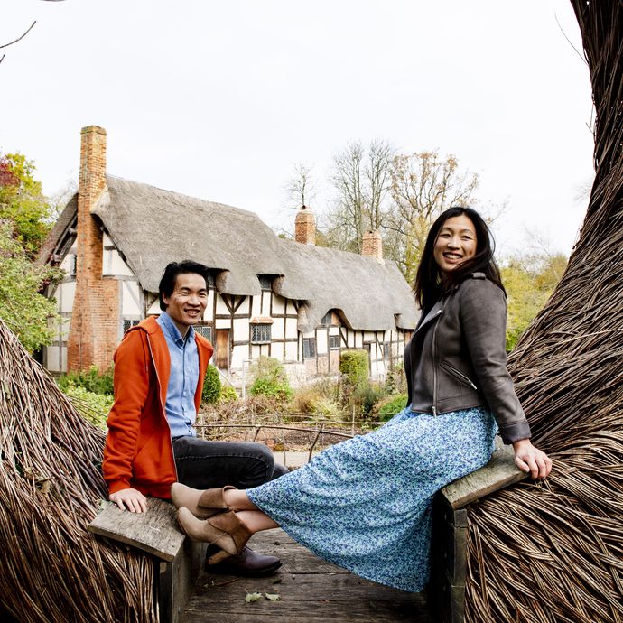Asian couple sitting on a wooden sculpture in Stratford-upon-Avon with Shakespeare's birthplace in the backdrop