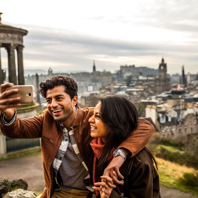 Couple taking a selfie on a mobile phone with Edinburgh in the background