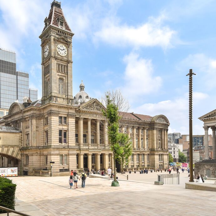 A square in Birmingham with crowds walking past ornate city buildings