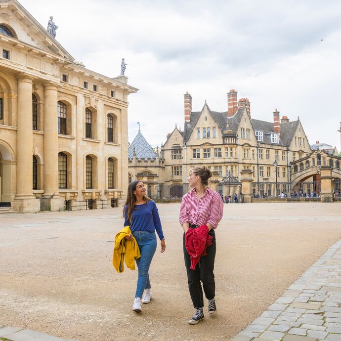 Two women walk across a courtyard among heritage buildings in Oxford